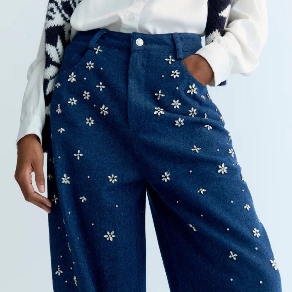 A stylish wide-leg denim pant featuring delicate hand-applied crystal details on the front for a subtle touch of sparkle. Designed with patch pockets at the back and finished with TNS embroidery on the waistband, it combines casual comfort with refined, unique details.  Model: Height 176 cm. Is wearing size S  Made in India  Color Collection: Blue Denim  100% Cotton